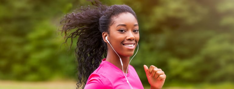 Une jeune femme noire aux cheveux naturels et un haut de sport rose qui fait son jogging