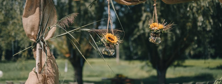 Rustikaler Traubogen im Freien, dekoriert mit Jute-Stoff und hängenden Sonnenblumenvasen 