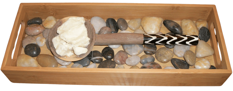 shea butter on wooden spoon on wooden tray with river rocks