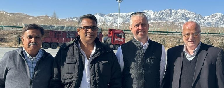 Businessmen posing outdoors with a logistics truck and snow-capped mountains in the background.