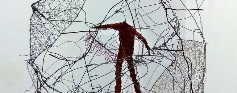 A modern wire sculpture featuring a red human figure suspended within a complex mesh cage.