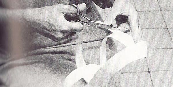 Close-up of hands using scissors to cut a strip of white paper ribbon in a black and white photo.