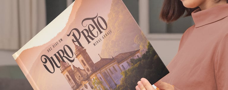 Mulher sorrindo ao folhear álbum de viagem personalizado de Ouro Preto na sala de estar.