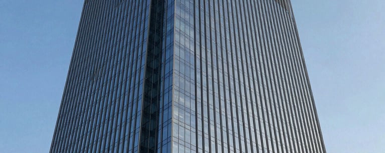 Exterior architectural rendering of a modern glass skyscraper. Sharp geometric lines against a clear blue sky. Reflective surfaces showing surrounding city architecture. Professional North American style.