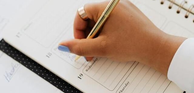 Mano con bolígrafo dorado escribiendo en una agenda especial