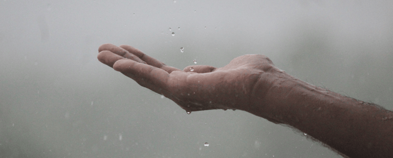 Hand met palm omhoog waarop regendruppels vallen, symbool voor voelen en korte reflectie.