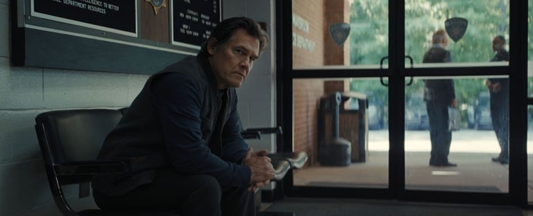 Josh Brolin sits pensively in a police station lobby, hands clasped, while two blurred figures talk