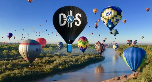 Colorful hot air balloons floating over the Rio Grande river in Albuquerque during a festival.
