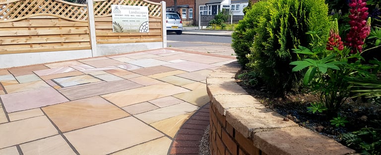 Colourful sandstone paving driveway and curved raised planter with colourful plants and flowers