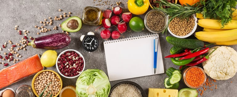 A colourful array of healthy food, vegetables and grains, with a notepad and pen and a clock in the middle