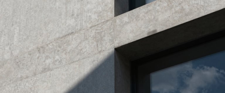 A close-up architectural detail of textured concrete and glass. Sophisticated play of shadow and light in midnight blue and cloud white. Modernist design aesthetic.