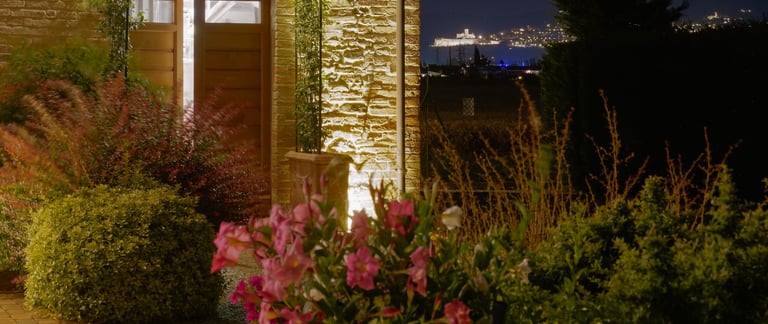 Esterno dell'agriturismo di sera, con fiori del nostro giardino e una romantica veduta su Assisi