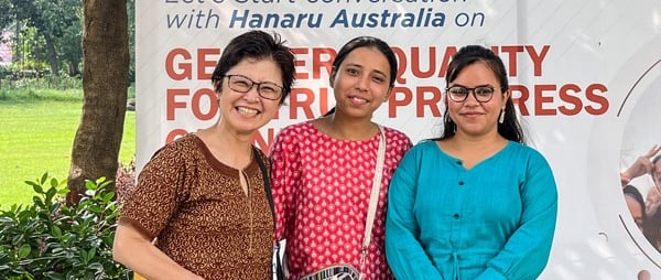 3 women in front of large placard