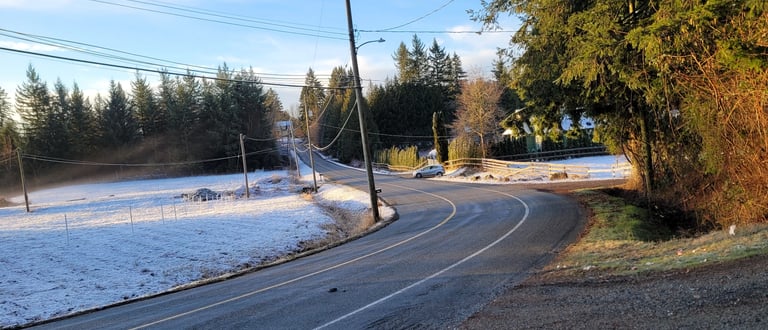 a curved country road with a snowy field on one side