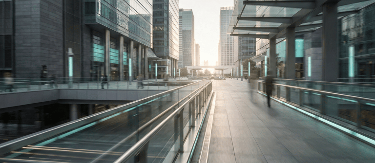 Modern glass office buildings and a pedestrian skywalk in a city business district at sunset.