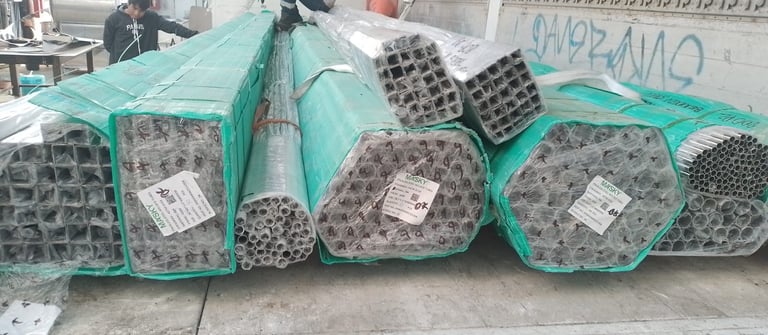 Bundles of stainless steel square and round tubing wrapped in green protective film for industrial delivery.