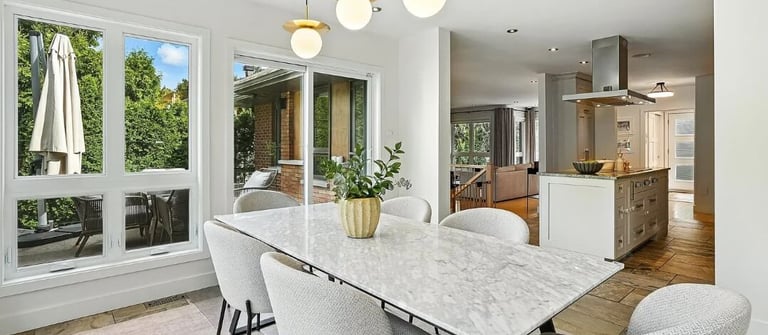Dining area with a marble table, upholstered chairs, and an open kitchen in the background.