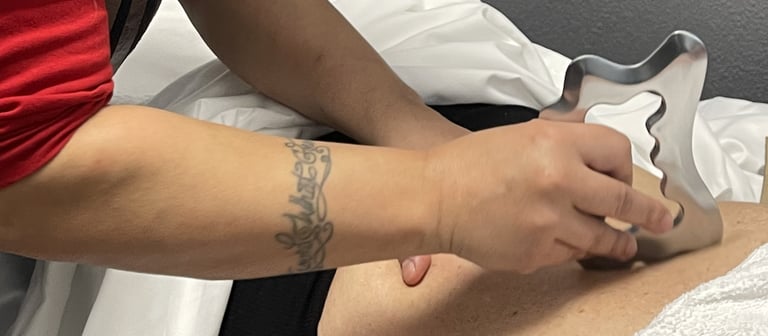 Therapist performing IASTM soft tissue mobilization on a patient's back using a metal scraping tool.