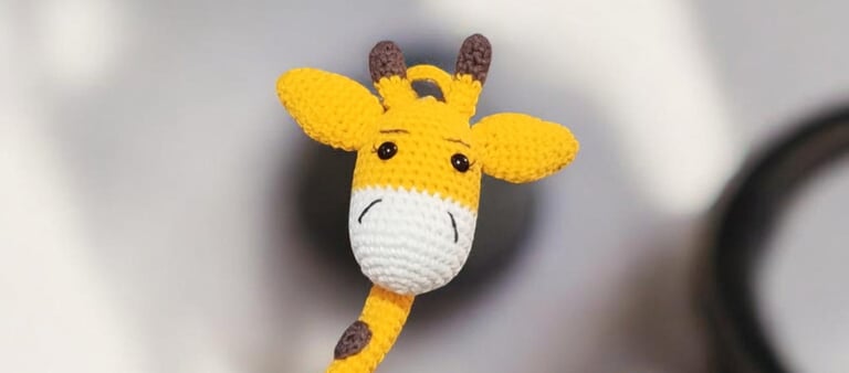Jirafa de juguete hecha a mano con ganchillo, con detalles de hilo amarillo y blanco.