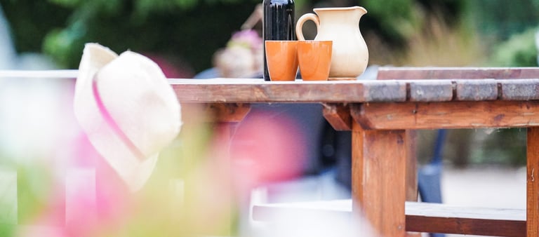 Tavolo nel giardino dell'agriturismo con sopra una caraffa, vino locale e bicchieri in terracotta