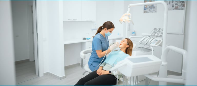Una dentista con mascarilla y uniforme azul examinando la boca de una paciente 