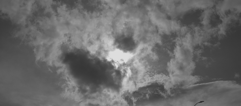Cielo nublado en blanco y negro con luz entre nubes y poste urbano