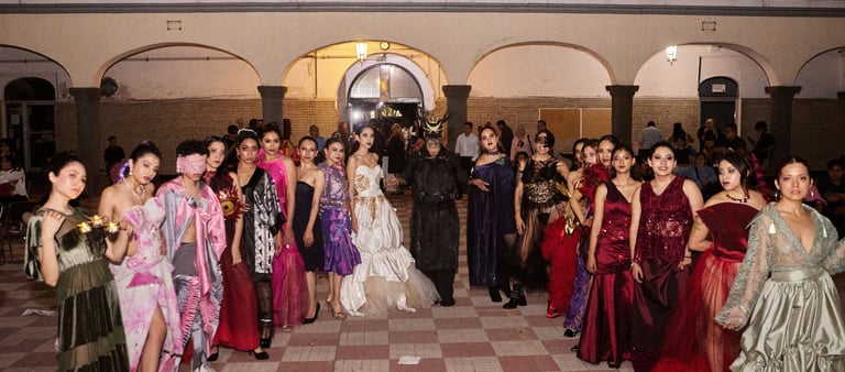 Fashion models posing in avant-garde designer gowns and creative costumes at an outdoor evening runway show.