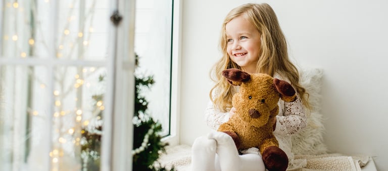 a little girl looking out the window sitting on a sofa with a teddy bear