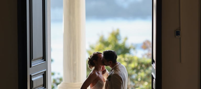 Newlyweds kiss on a balcony overlooking water, framed by open doors Elaine Brackin, Kenan Kasap