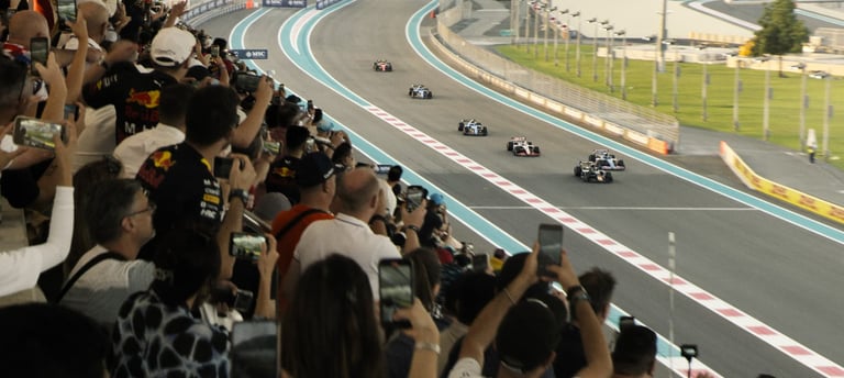 "Fans crowd the grandstand and hold up phones as Formula 1 cars race down the Yas Marina Circuit tra