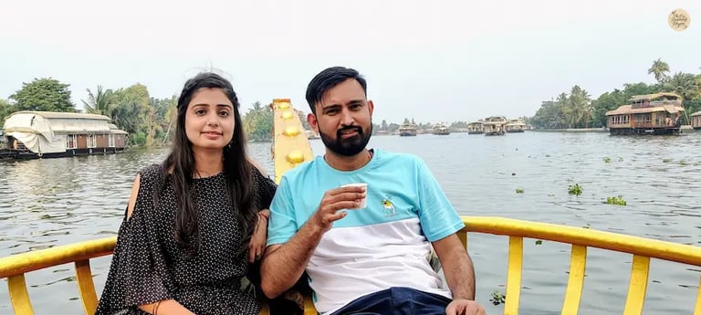 Couple enjoying tea on a traditional houseboat while cruising across Vembanad Lake in Alleppey, Kerala.