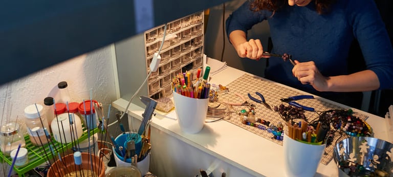 Joyera utilizando pinzas en una mesa de trabajo artesanal equipada con cuentas y varillas de vidrio.