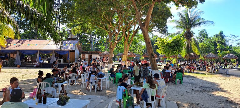 Crowd dining outdoors under palm trees under the shade at Centro Recreacional Mokanranko
