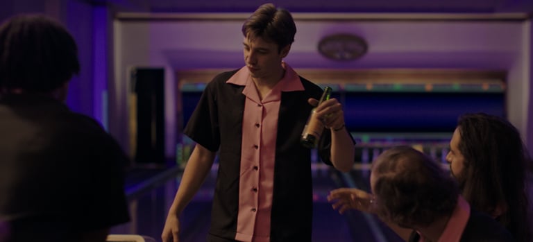 a man in a bowling shirt is holding a bottle of beer