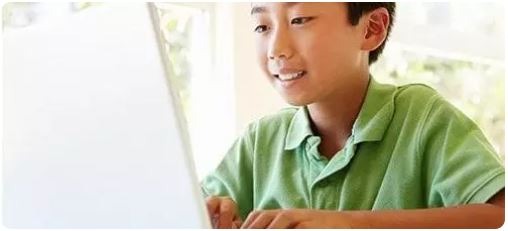 A young Asian boy smiling while using a laptop for remote learning and education.