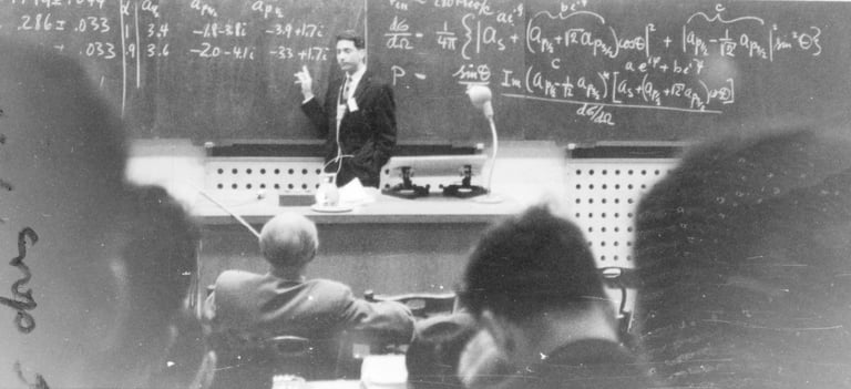 Vintage black and white photo of a professor teaching physics equations on a chalkboard.