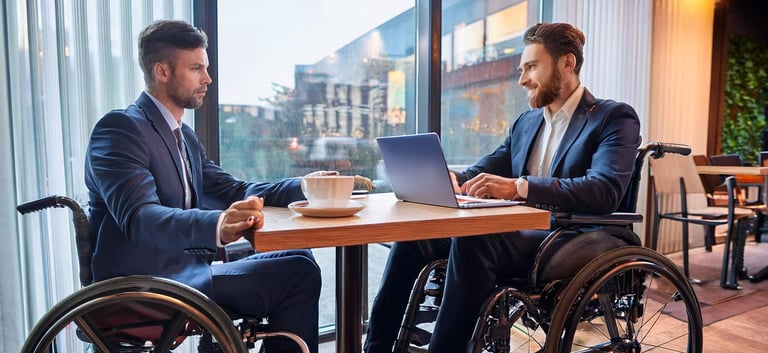 Zwei Rollstuhlfahrer sitzen für ein Beratungsgespräch in einem Café