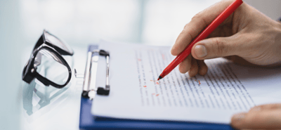 A person holding a pen and writing on a paper representing editing and proofreading