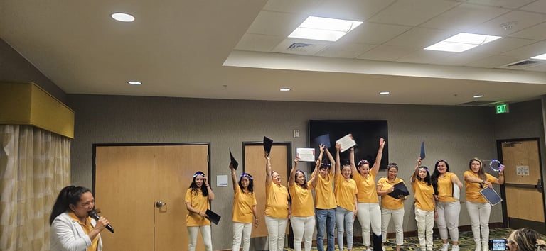 Smiling graduates in yellow shirts hold up diplomas during a celebratory graduation ceremony.