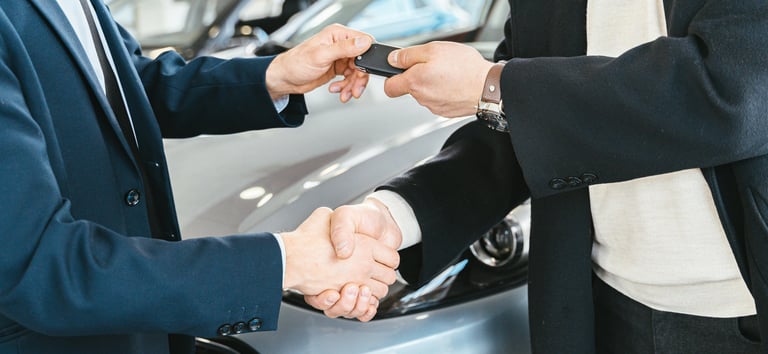Remise de clés avec poignée de main entre deux personnes devant une voiture.