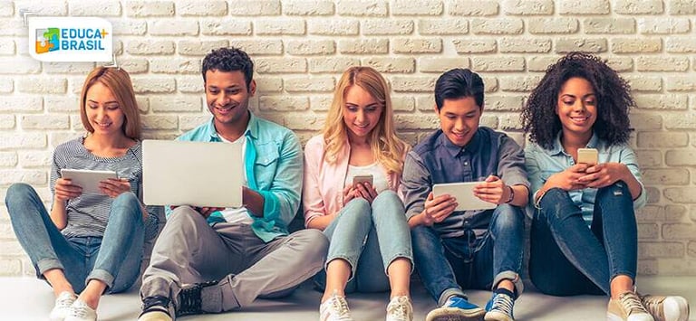 imagem retrata um grupo de estudantes mexendo em seus celulares e computadores