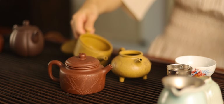 Person pouring water from a teapot with cups and a tea strainer on a wooden table