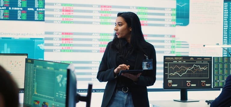 DataOps analyst using tablet in front of a board of data screens