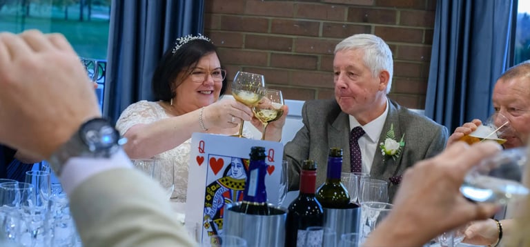 Smiling bride and groom toast with wine glasses at their wedding reception dinner table.