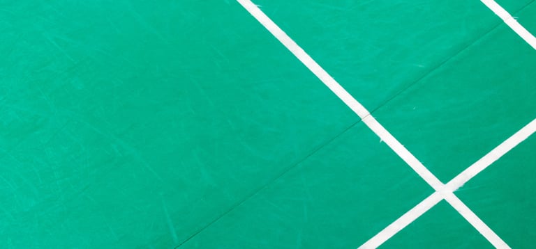 Top down view of a green badminton court surface with white boundary line markings.