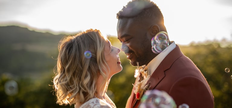 a bride and groom in front of blowing bubbles in the air, in front of the sunset