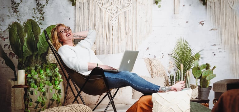 a tattooed corporate woman laughing sitting in a chair with a laptop