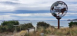 Verdigris metal globe sculpture on the beach with a mother whale and her calf in the middle of it