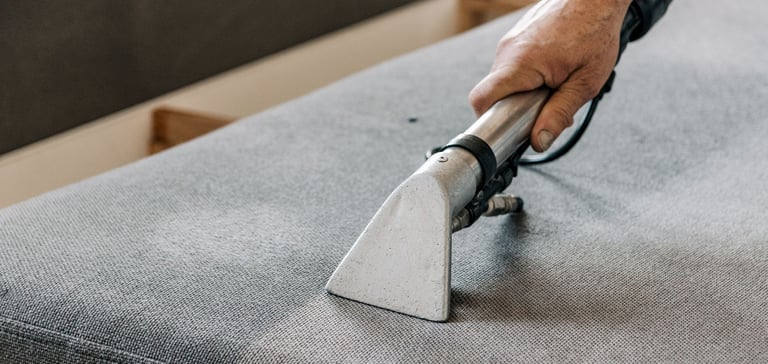 Professional upholstery cleaning sofa using a steam vacuum tool for stain removal.