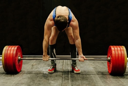 Male athlete preparing for a deadlift with a heavy barbell and red weight plates.